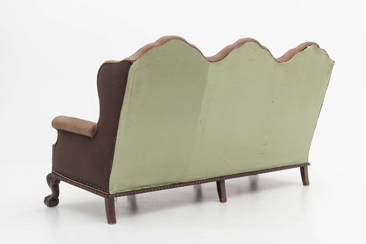 Sofa med trekk vevd av Ulrikke Greve. Vevnaden er vevet spesielt til denne sofaen. Det  er nyere stoff-trekk på armlenene. Møbeltrekket er nå stiftet fast med stiftemaskin; antagelig en reparasjon, og dekorert med pyntestift i messing.