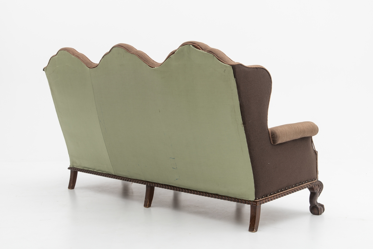 Sofa med trekk vevd av Ulrikke Greve. Vevnaden er vevet spesielt til denne sofaen. Det  er nyere stoff-trekk på armlenene. Møbeltrekket er nå stiftet fast med stiftemaskin; antagelig en reparasjon, og dekorert med pyntestift i messing.