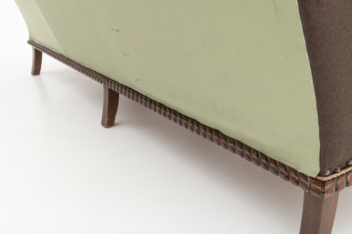 Sofa med trekk vevd av Ulrikke Greve. Vevnaden er vevet spesielt til denne sofaen. Det  er nyere stoff-trekk på armlenene. Møbeltrekket er nå stiftet fast med stiftemaskin; antagelig en reparasjon, og dekorert med pyntestift i messing.