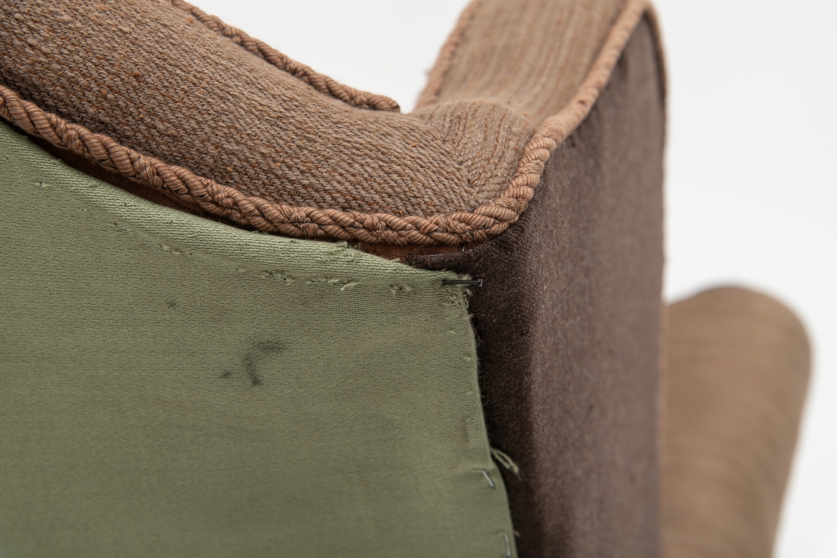 Sofa med trekk vevd av Ulrikke Greve. Vevnaden er vevet spesielt til denne sofaen. Det  er nyere stoff-trekk på armlenene. Møbeltrekket er nå stiftet fast med stiftemaskin; antagelig en reparasjon, og dekorert med pyntestift i messing.