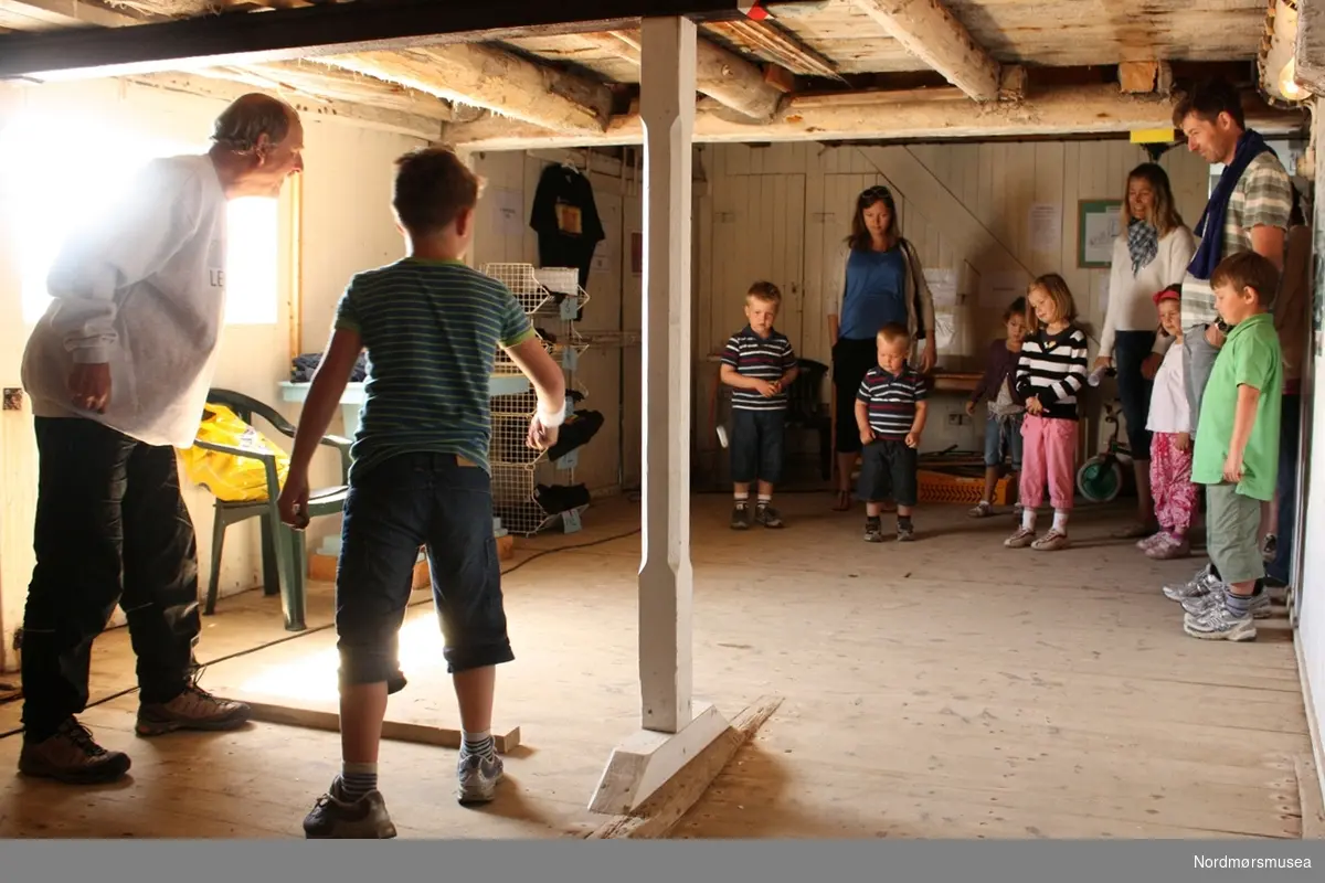 Tor Larsen instruerer i å kaste 'blekkskiv'. Arrangementsfoto fra "Familiedagen" i regi av Nordmøre museum på Milnbrygga, Gomalandet i Kristiansund. Bildet er datert 21. juni 2009. Fotograf er Roar Leite ved Nordmøre museum. Fra Nordmøre museums fotosamlinger.