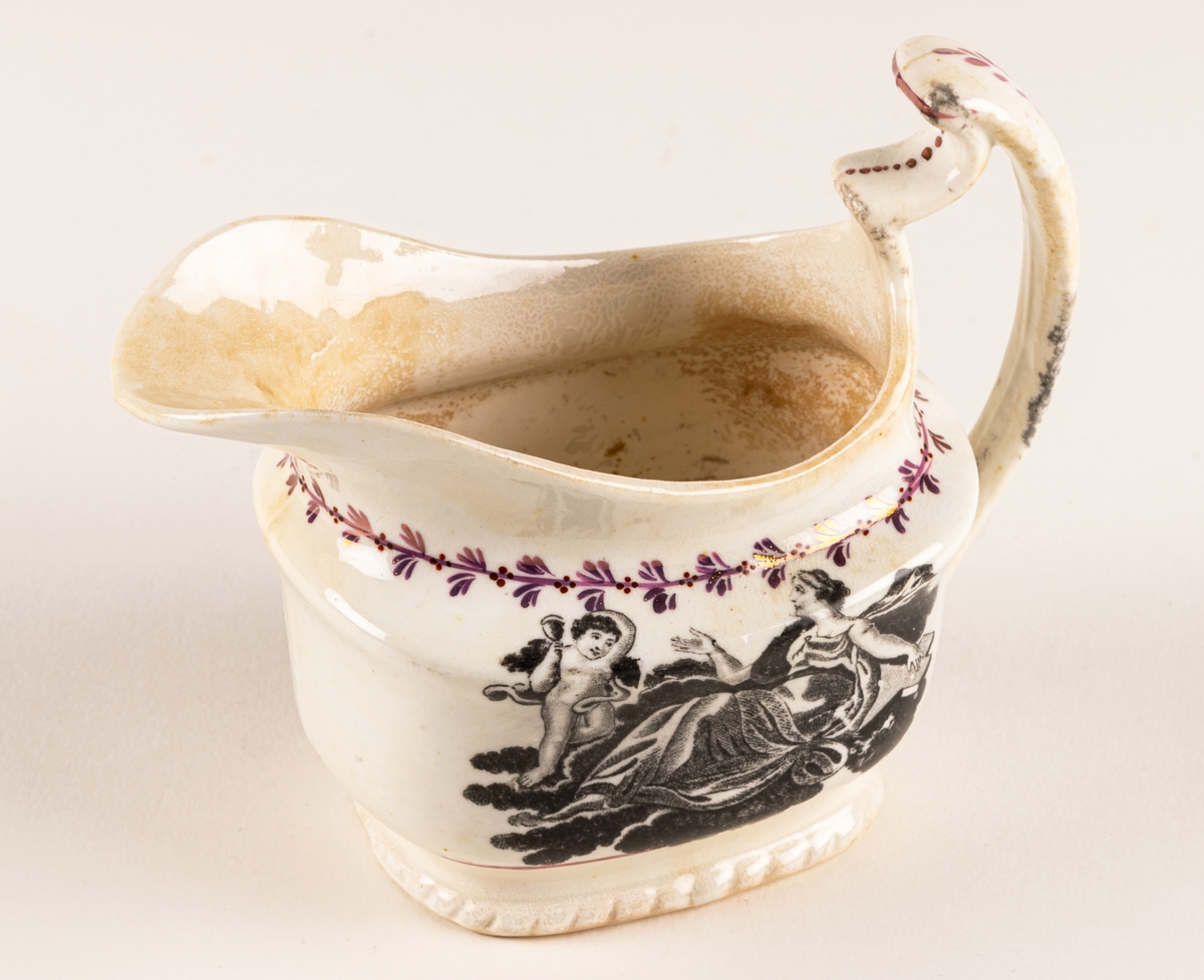 Gräddkanna av engelskt flintgods med rosa lyster. Dekor: allegoriska figurer i svart, samt röda växtband. Text "Faith & Hope".