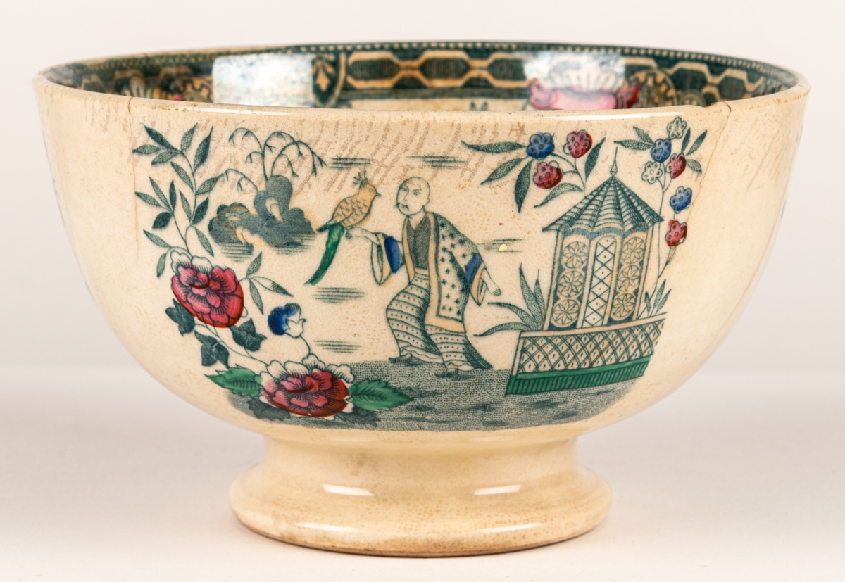 Spillkum, porslin, dekor med kinesiska motiv. Vit med bårder och blommor samt figurscenerier (schablon) i blått, grönt, rött och guld. Stämpel i godset liknande "E 1".