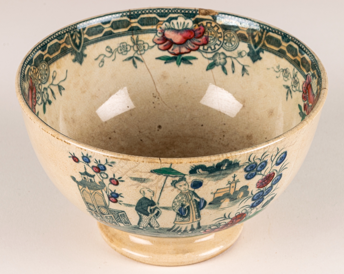 Spillkum, porslin, dekor med kinesiska motiv. Vit med bårder och blommor samt figurscenerier (schablon) i blått, grönt, rött och guld. Stämpel i godset liknande "E 1".