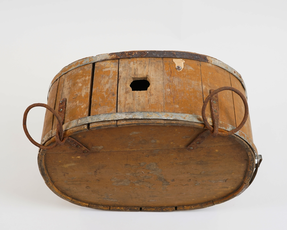 Mjølkeflaske/ kløvflaske. I tre. Oval form. Lagga. To metall band rundt. Måla med okerfarga måling. To jarnringer på eine sida nytta til feste ved bering/ frakting med hest (kløv).