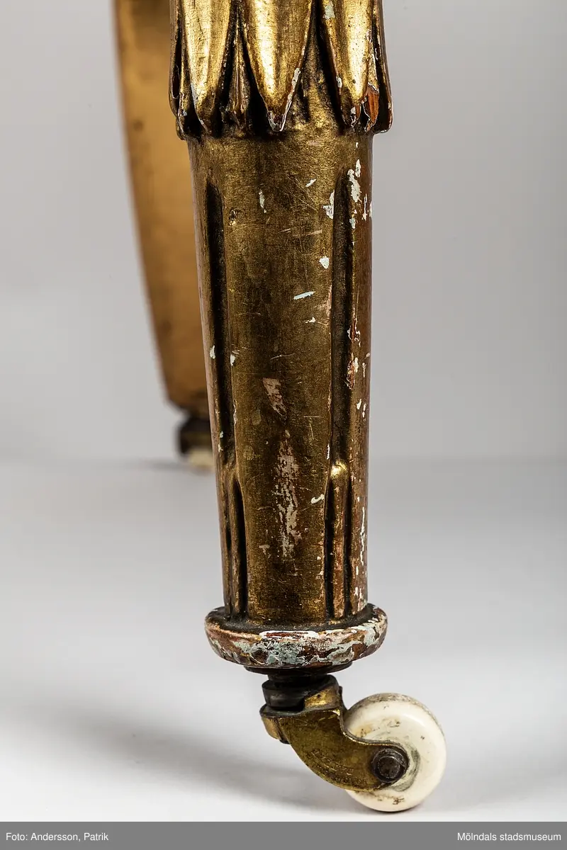 Fåtölj, s.k. "baljfåtölj", sengustaviansk, tillverkad omkring år 1800. 

Kraftigt svängd rygg, raka sarger med skuren dekor, svarvade, bladhölstrade och kannelerade framben, sabelformade bakben. 
Fast stoppad sits och rygg, med sliten, senare klädsel i grönrandigt siden. Bevarad originalstoppning.

Senare bemålning i guld. Äldre rödbrun färg kan anas under förgyllningen.
Benen har kortats av och kompletterats med trissor (hjul) i mässing under 1800-talets andra hälft.

Sitthöjd 440 mm, Bredd 610 mm.
Material: Björk, Tageltyg, Sadelgjord.

Fåtöljen är en av ett par. Båda är signerade med brännstämpel AIS på den bakre sargen. Det finns fyra kända snickare i Lindome som använde signaturen AIS – Anders Johansson i Hassungared (1780-1847), Anders Jonsson i Ingemantorp (1770-1832), Anders Jönsson i Gastorp (1778-1858) och Andreas Johansson i Skår (1793-1871).

Inköpt på Kungsbacka Auktionskammare.
Samhör med MM05442