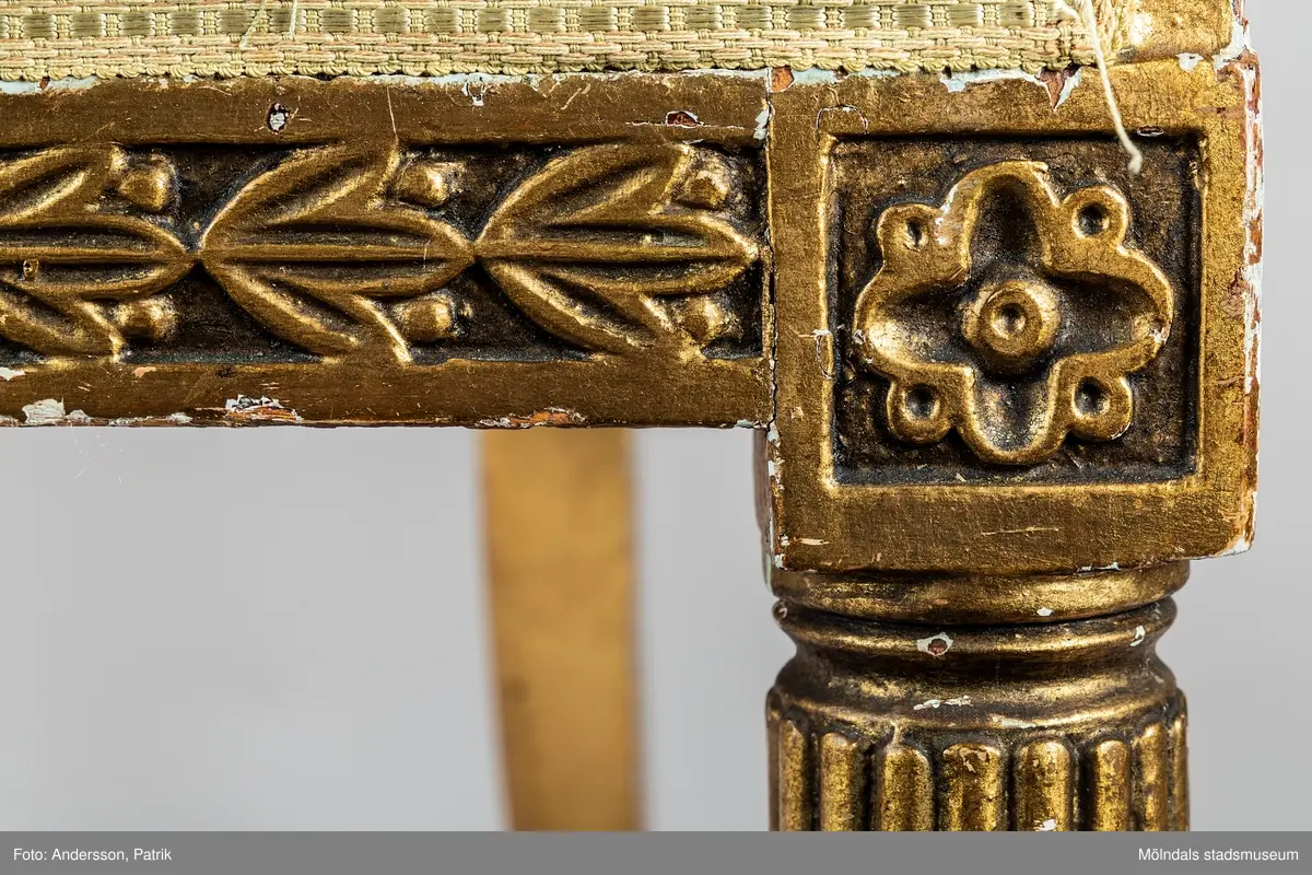 Fåtölj, s.k. "baljfåtölj", sengustaviansk, tillverkad omkring år 1800. 

Kraftigt svängd rygg, raka sarger med skuren dekor, svarvade, bladhölstrade och kannelerade framben, sabelformade bakben. 
Fast stoppad sits och rygg, med sliten, senare klädsel i grönrandigt siden. Bevarad originalstoppning.

Senare bemålning i guld. Äldre rödbrun färg kan anas under förgyllningen.
Benen har kortats av och kompletterats med trissor (hjul) i mässing under 1800-talets andra hälft.

Sitthöjd 440 mm, Bredd 610 mm.
Material: Björk, Tageltyg, Sadelgjord.

Fåtöljen är en av ett par. Båda är signerade med brännstämpel AIS på den bakre sargen. Det finns fyra kända snickare i Lindome som använde signaturen AIS – Anders Johansson i Hassungared (1780-1847), Anders Jonsson i Ingemantorp (1770-1832), Anders Jönsson i Gastorp (1778-1858) och Andreas Johansson i Skår (1793-1871).

Inköpt på Kungsbacka Auktionskammare.
Samhör med MM05442