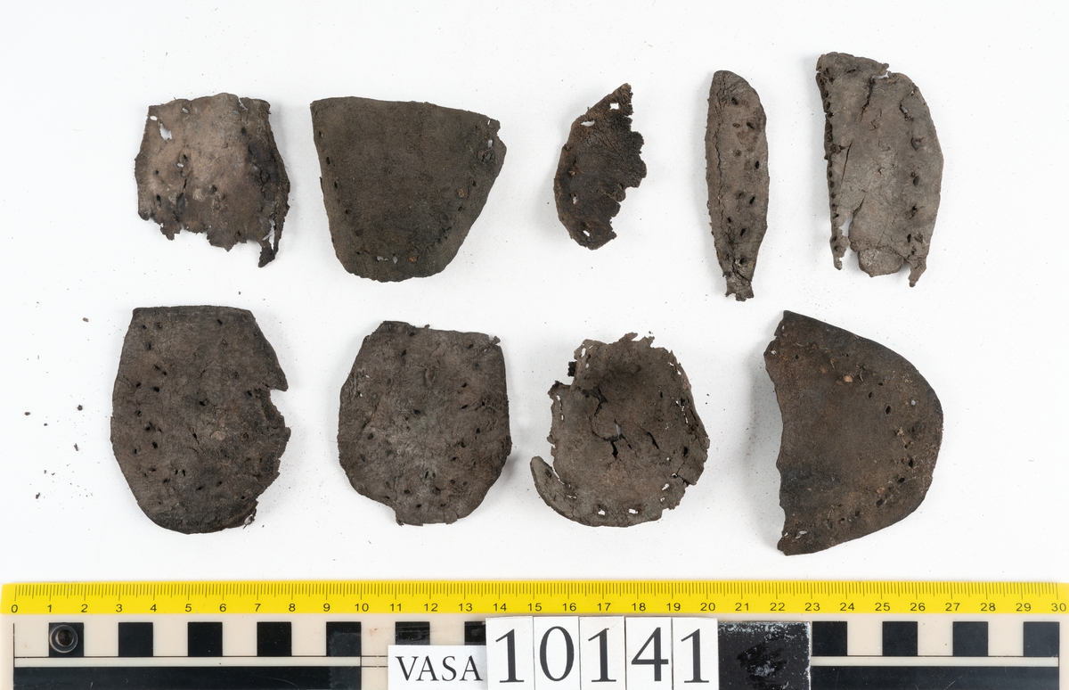 Ett 70-tal delar och fragment av sko: del av skobotten, inlägg, sulor, ovanläder, sidostycken m.m. samt tre fragment textilband samt ett fragment av filt eller tuskaftsväv.

Skobotten, troligtvis från en höger sko. Klacken är uppbyggd av fem klacklappar samt inlägg. Klacken är ritsad på undersidan. Skobottnen har kvarsittande skopligg.

På delarna och fragmenten finns hål efter skopligg och tråd. Lädret är mycket sprött samt har mineral- och rostliknande utfällningar.