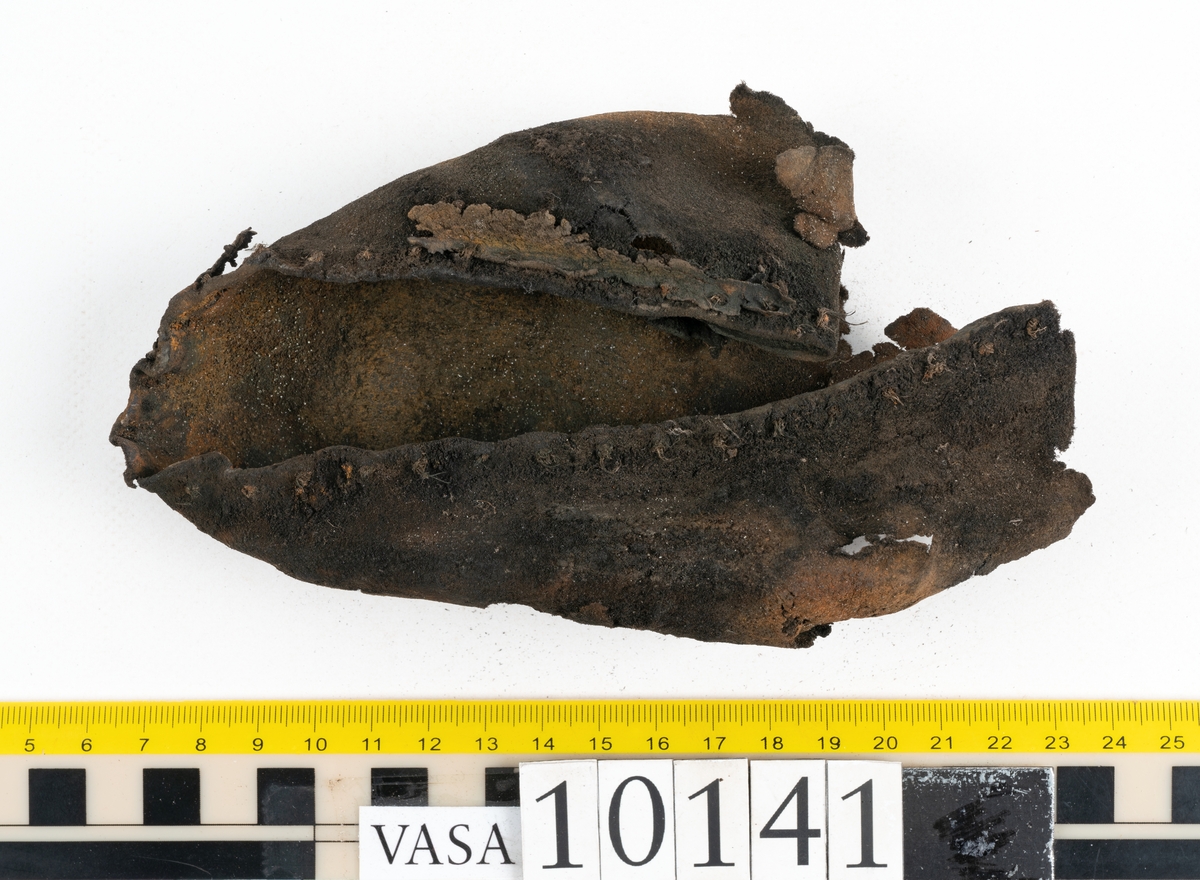 Ett 70-tal delar och fragment av sko: del av skobotten, inlägg, sulor, ovanläder, sidostycken m.m. samt tre fragment textilband samt ett fragment av filt eller tuskaftsväv.

Skobotten, troligtvis från en höger sko. Klacken är uppbyggd av fem klacklappar samt inlägg. Klacken är ritsad på undersidan. Skobottnen har kvarsittande skopligg.

På delarna och fragmenten finns hål efter skopligg och tråd. Lädret är mycket sprött samt har mineral- och rostliknande utfällningar.