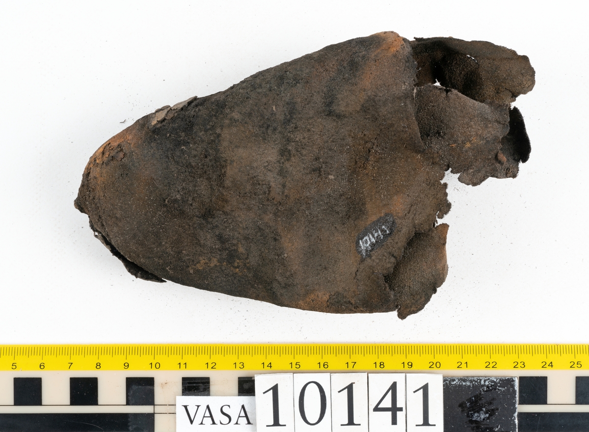 Ett 70-tal delar och fragment av sko: del av skobotten, inlägg, sulor, ovanläder, sidostycken m.m. samt tre fragment textilband samt ett fragment av filt eller tuskaftsväv.

Skobotten, troligtvis från en höger sko. Klacken är uppbyggd av fem klacklappar samt inlägg. Klacken är ritsad på undersidan. Skobottnen har kvarsittande skopligg.

På delarna och fragmenten finns hål efter skopligg och tråd. Lädret är mycket sprött samt har mineral- och rostliknande utfällningar.