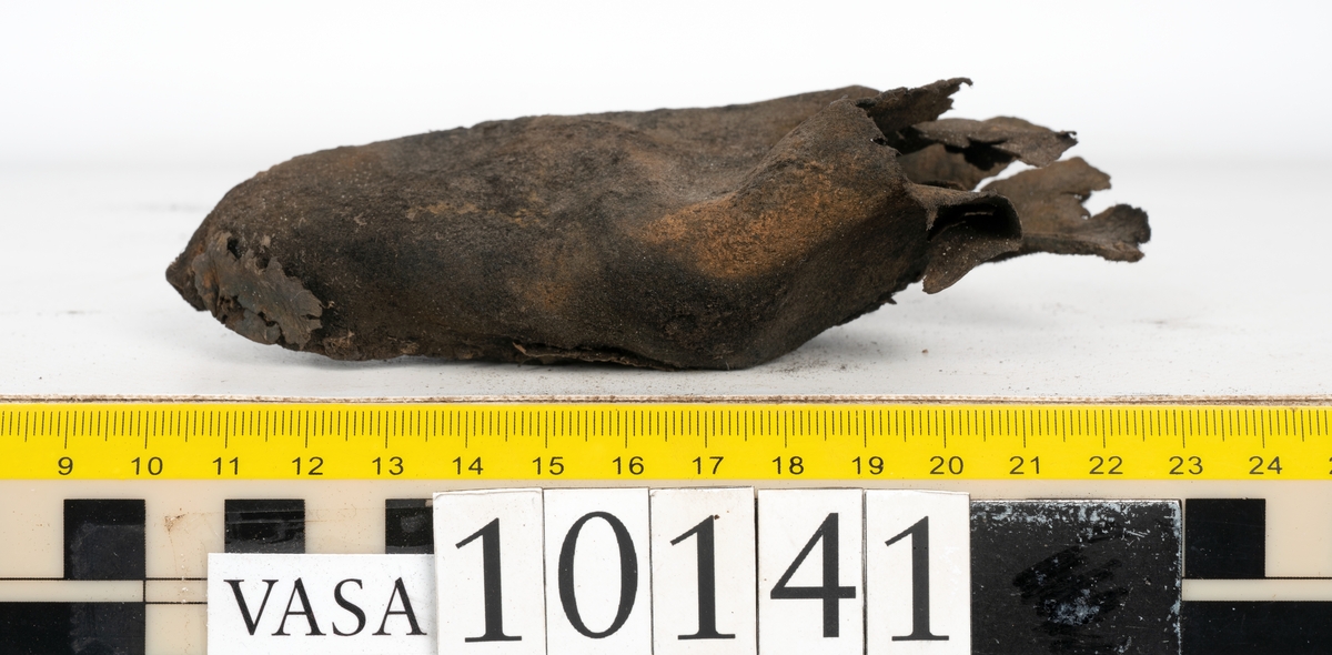Ett 70-tal delar och fragment av sko: del av skobotten, inlägg, sulor, ovanläder, sidostycken m.m. samt tre fragment textilband samt ett fragment av filt eller tuskaftsväv.

Skobotten, troligtvis från en höger sko. Klacken är uppbyggd av fem klacklappar samt inlägg. Klacken är ritsad på undersidan. Skobottnen har kvarsittande skopligg.

På delarna och fragmenten finns hål efter skopligg och tråd. Lädret är mycket sprött samt har mineral- och rostliknande utfällningar.