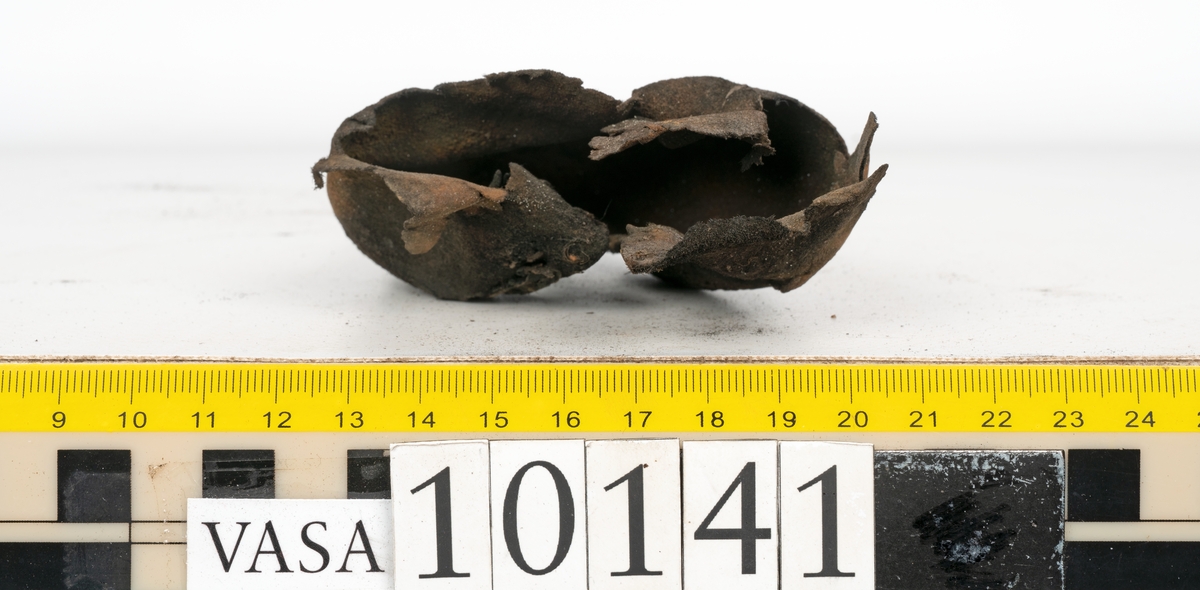 Ett 70-tal delar och fragment av sko: del av skobotten, inlägg, sulor, ovanläder, sidostycken m.m. samt tre fragment textilband samt ett fragment av filt eller tuskaftsväv.

Skobotten, troligtvis från en höger sko. Klacken är uppbyggd av fem klacklappar samt inlägg. Klacken är ritsad på undersidan. Skobottnen har kvarsittande skopligg.

På delarna och fragmenten finns hål efter skopligg och tråd. Lädret är mycket sprött samt har mineral- och rostliknande utfällningar.