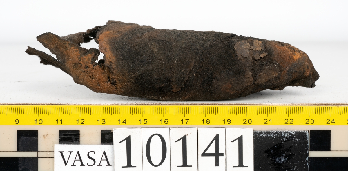 Ett 70-tal delar och fragment av sko: del av skobotten, inlägg, sulor, ovanläder, sidostycken m.m. samt tre fragment textilband samt ett fragment av filt eller tuskaftsväv.

Skobotten, troligtvis från en höger sko. Klacken är uppbyggd av fem klacklappar samt inlägg. Klacken är ritsad på undersidan. Skobottnen har kvarsittande skopligg.

På delarna och fragmenten finns hål efter skopligg och tråd. Lädret är mycket sprött samt har mineral- och rostliknande utfällningar.