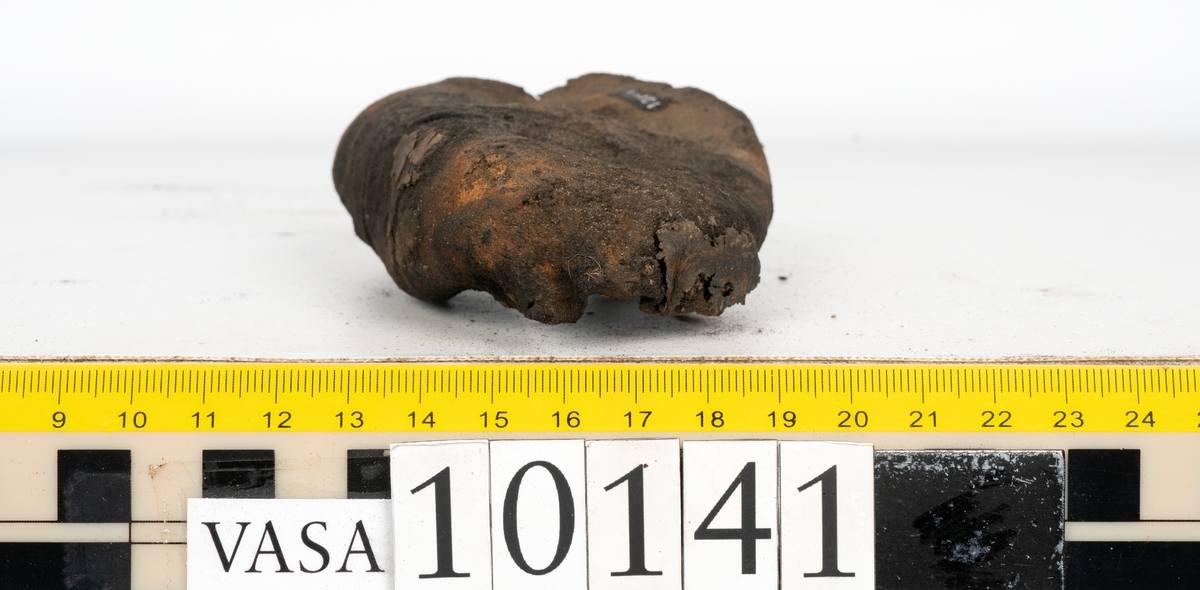 Ett 70-tal delar och fragment av sko: del av skobotten, inlägg, sulor, ovanläder, sidostycken m.m. samt tre fragment textilband samt ett fragment av filt eller tuskaftsväv.

Skobotten, troligtvis från en höger sko. Klacken är uppbyggd av fem klacklappar samt inlägg. Klacken är ritsad på undersidan. Skobottnen har kvarsittande skopligg.

På delarna och fragmenten finns hål efter skopligg och tråd. Lädret är mycket sprött samt har mineral- och rostliknande utfällningar.