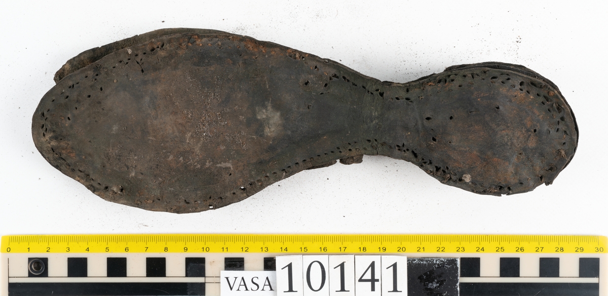 Ett 70-tal delar och fragment av sko: del av skobotten, inlägg, sulor, ovanläder, sidostycken m.m. samt tre fragment textilband samt ett fragment av filt eller tuskaftsväv.

Skobotten, troligtvis från en höger sko. Klacken är uppbyggd av fem klacklappar samt inlägg. Klacken är ritsad på undersidan. Skobottnen har kvarsittande skopligg.

På delarna och fragmenten finns hål efter skopligg och tråd. Lädret är mycket sprött samt har mineral- och rostliknande utfällningar.