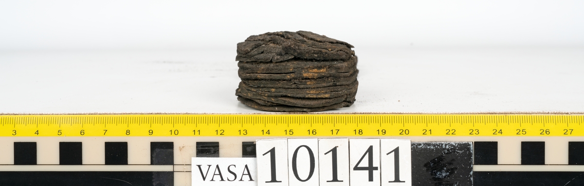 Ett 70-tal delar och fragment av sko: del av skobotten, inlägg, sulor, ovanläder, sidostycken m.m. samt tre fragment textilband samt ett fragment av filt eller tuskaftsväv.

Skobotten, troligtvis från en höger sko. Klacken är uppbyggd av fem klacklappar samt inlägg. Klacken är ritsad på undersidan. Skobottnen har kvarsittande skopligg.

På delarna och fragmenten finns hål efter skopligg och tråd. Lädret är mycket sprött samt har mineral- och rostliknande utfällningar.