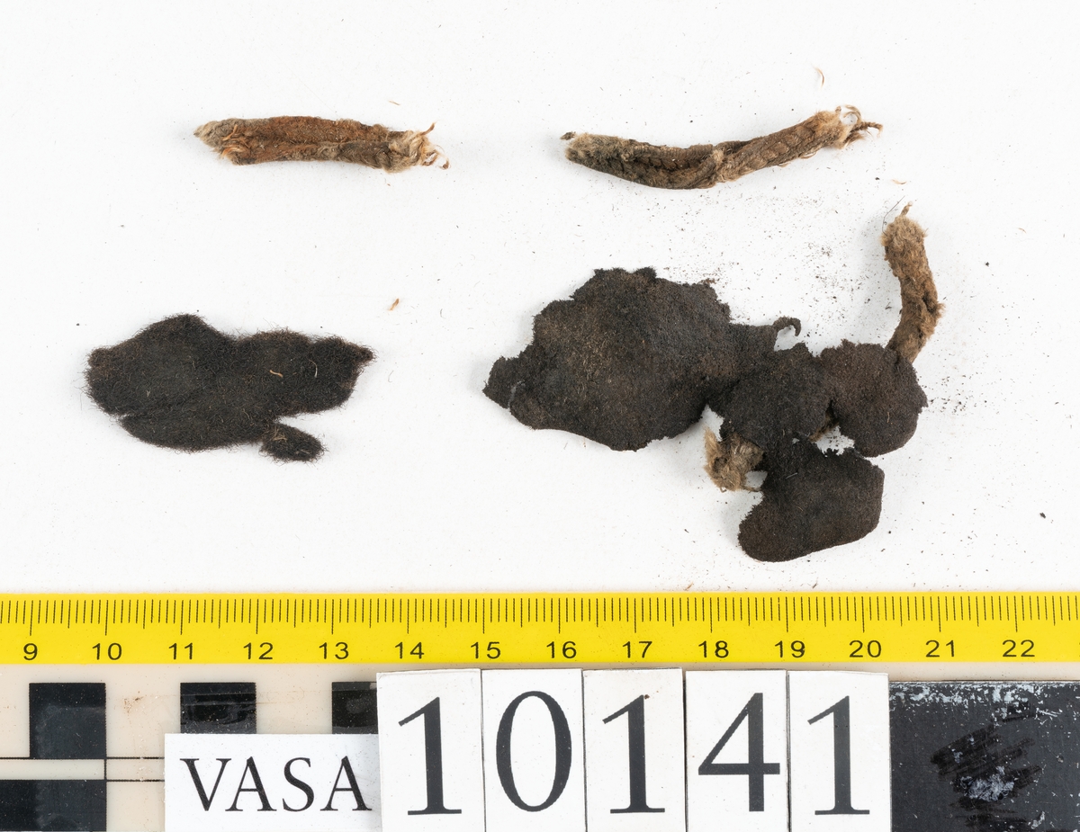 Ett 70-tal delar och fragment av sko: del av skobotten, inlägg, sulor, ovanläder, sidostycken m.m. samt tre fragment textilband samt ett fragment av filt eller tuskaftsväv.

Skobotten, troligtvis från en höger sko. Klacken är uppbyggd av fem klacklappar samt inlägg. Klacken är ritsad på undersidan. Skobottnen har kvarsittande skopligg.

På delarna och fragmenten finns hål efter skopligg och tråd. Lädret är mycket sprött samt har mineral- och rostliknande utfällningar.