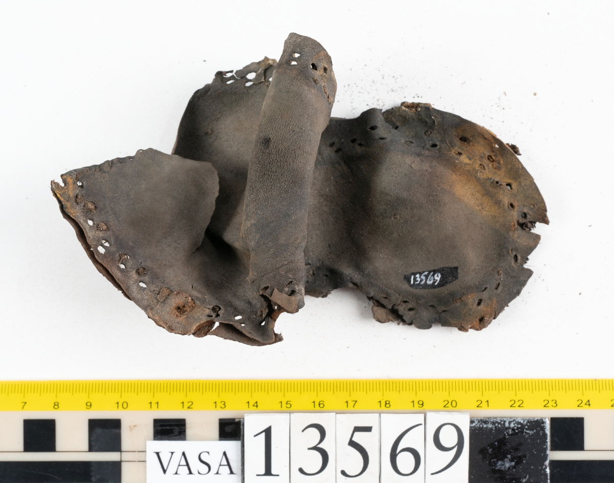Ett 30-tal delar och fragment av sko: delar av inlägg, ovanläder, klack och sulor.

Ett ovanläder med kvarsittande tråd. Lädret är spaltat samt har rostliknande utfällningar. Två fragmentariska sulor med kvarsittande pligg. På flertalet fragment syns vita och rostliknande utfällningar.