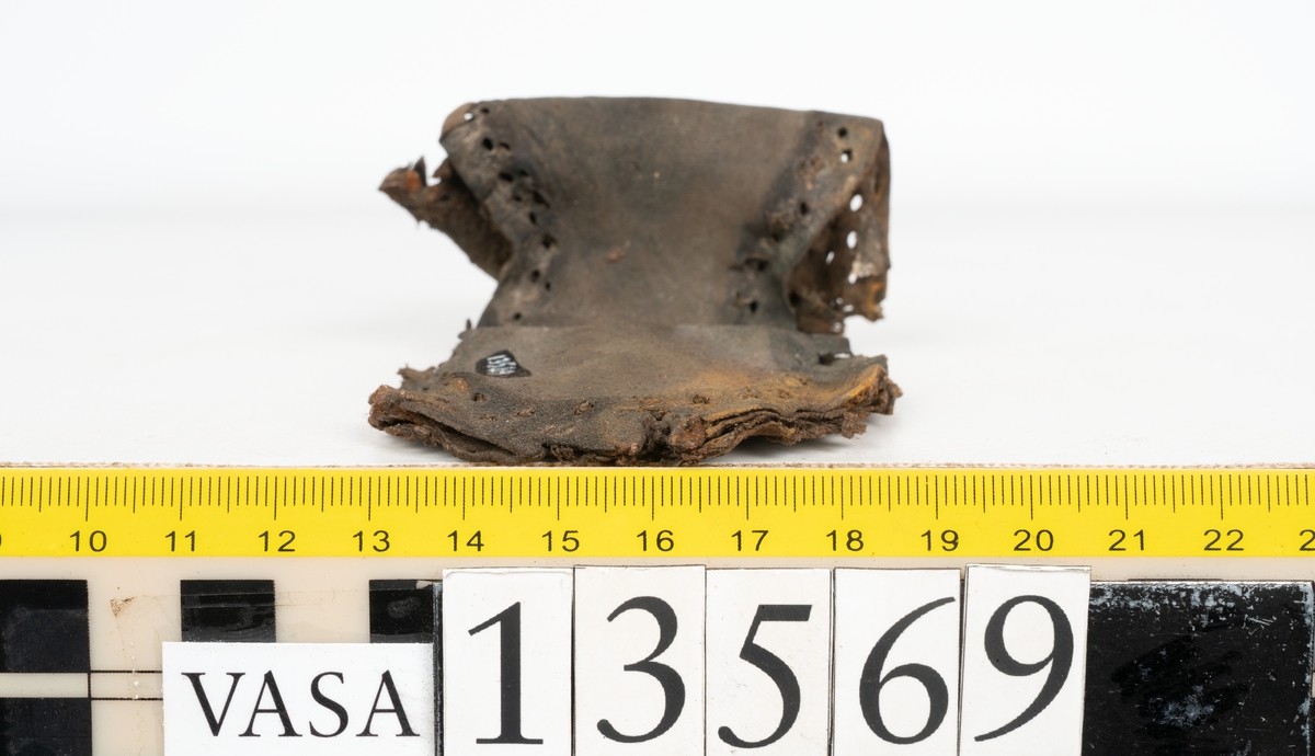 Ett 30-tal delar och fragment av sko: delar av inlägg, ovanläder, klack och sulor.

Ett ovanläder med kvarsittande tråd. Lädret är spaltat samt har rostliknande utfällningar. Två fragmentariska sulor med kvarsittande pligg. På flertalet fragment syns vita och rostliknande utfällningar.