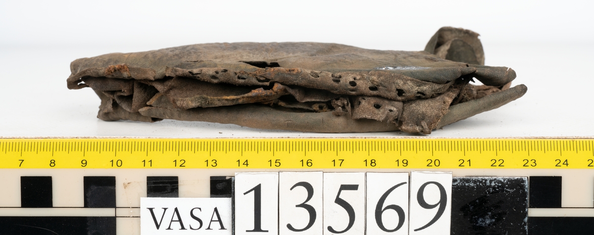 Ett 30-tal delar och fragment av sko: delar av inlägg, ovanläder, klack och sulor.

Ett ovanläder med kvarsittande tråd. Lädret är spaltat samt har rostliknande utfällningar. Två fragmentariska sulor med kvarsittande pligg. På flertalet fragment syns vita och rostliknande utfällningar.