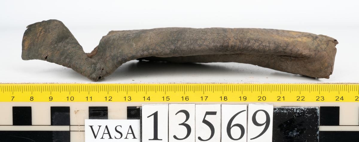 Ett 30-tal delar och fragment av sko: delar av inlägg, ovanläder, klack och sulor.

Ett ovanläder med kvarsittande tråd. Lädret är spaltat samt har rostliknande utfällningar. Två fragmentariska sulor med kvarsittande pligg. På flertalet fragment syns vita och rostliknande utfällningar.