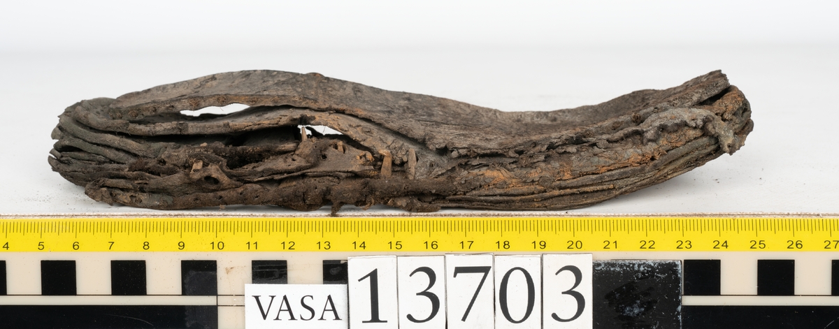 Delar och fragment av sko: ovanläder, skobotten, sula, skopligg samt fragment.

Ovanlädret är fragmentariskt och spaltad samt har rostfärgade utfällningar.

Skobottnen har kvarsittande skopligg och tråd. Klacken är uppbyggd av tre eller fyra klacklappar. Lädret har en grå beläggning, troligtvis av lera, samt rostfärgade utfällningar.

En sula med kvarsittande tråd. Lädret till sulan är kraftig.

Totalt fyra löst liggande skopligg och nio fragment/delar.