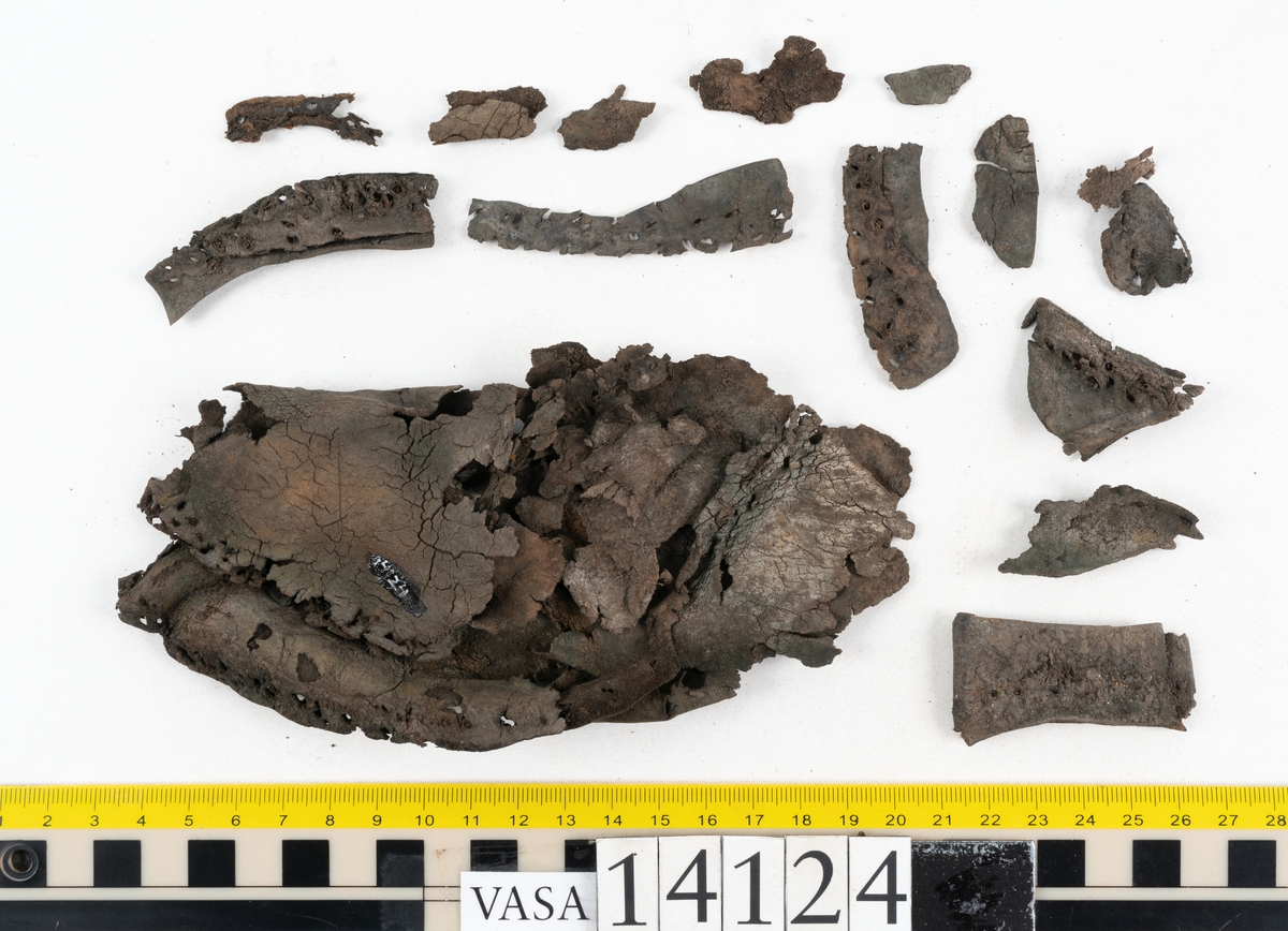 Sandalsydd högersko, troligtvis toffel, i delar.

Skobottnen består av två sulor med kvarsittanda skopligg och tråd. Vid tåpartiet sitter laglappar. På undersidan av yttersulan syns rostfärgade utfällningar.

Elva fragment från bottnen: sulor m m.

Ett fragmentariskt ovanläder. Ovanlädret har vita och rostfärgade utfällningar samt ligger hopvikt. Lädret är mycket sprött.
Totalt 15 fragment.