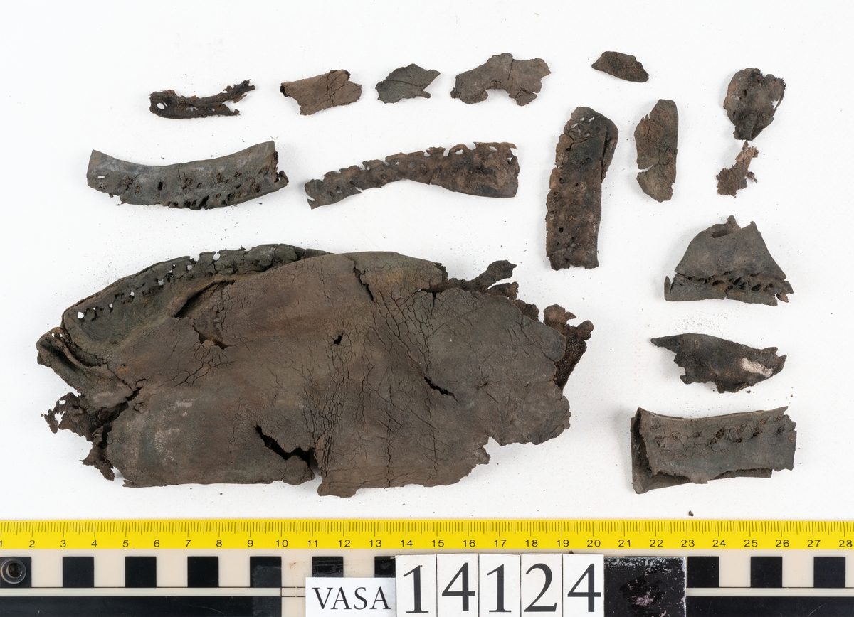 Sandalsydd högersko, troligtvis toffel, i delar.

Skobottnen består av två sulor med kvarsittanda skopligg och tråd. Vid tåpartiet sitter laglappar. På undersidan av yttersulan syns rostfärgade utfällningar.

Elva fragment från bottnen: sulor m m.

Ett fragmentariskt ovanläder. Ovanlädret har vita och rostfärgade utfällningar samt ligger hopvikt. Lädret är mycket sprött.
Totalt 15 fragment.