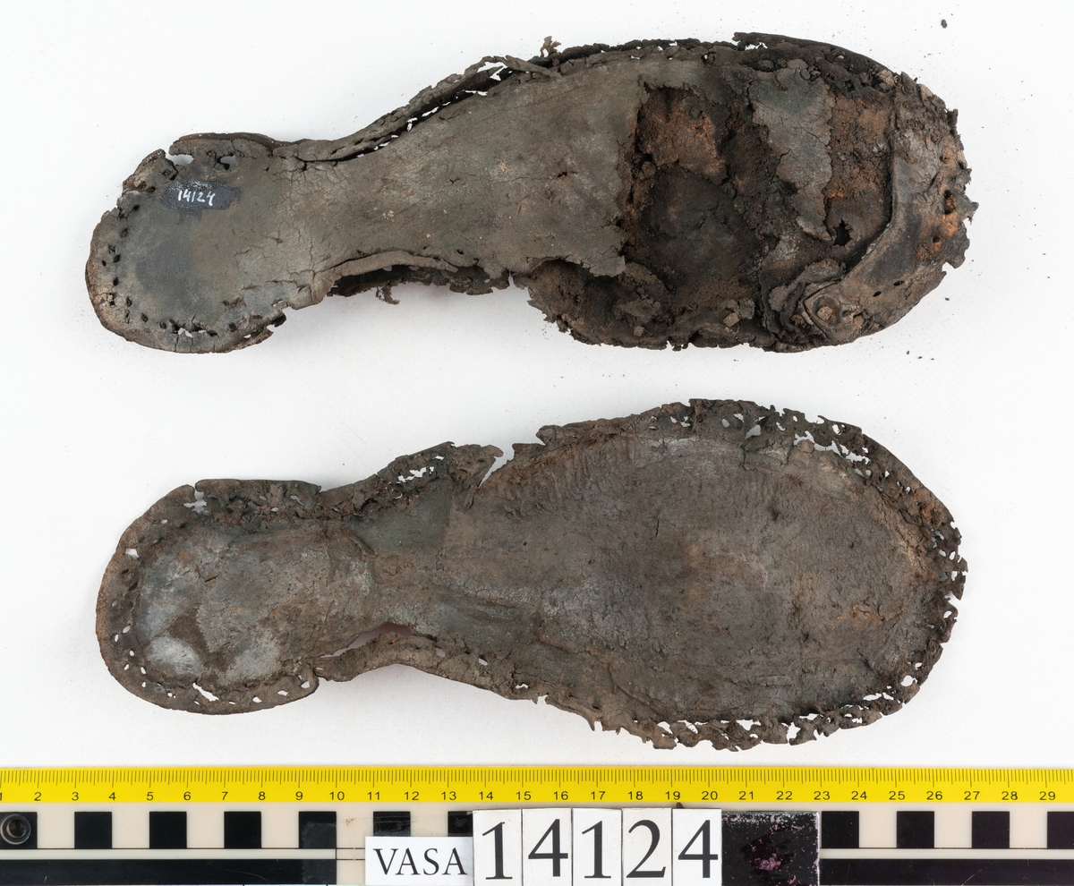 Sandalsydd högersko, troligtvis toffel, i delar.

Skobottnen består av två sulor med kvarsittanda skopligg och tråd. Vid tåpartiet sitter laglappar. På undersidan av yttersulan syns rostfärgade utfällningar.

Elva fragment från bottnen: sulor m m.

Ett fragmentariskt ovanläder. Ovanlädret har vita och rostfärgade utfällningar samt ligger hopvikt. Lädret är mycket sprött.
Totalt 15 fragment.