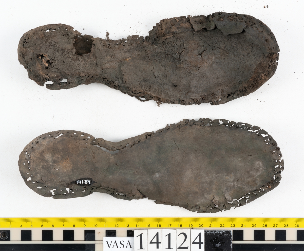 Sandalsydd högersko, troligtvis toffel, i delar.

Skobottnen består av två sulor med kvarsittanda skopligg och tråd. Vid tåpartiet sitter laglappar. På undersidan av yttersulan syns rostfärgade utfällningar.

Elva fragment från bottnen: sulor m m.

Ett fragmentariskt ovanläder. Ovanlädret har vita och rostfärgade utfällningar samt ligger hopvikt. Lädret är mycket sprött.
Totalt 15 fragment.