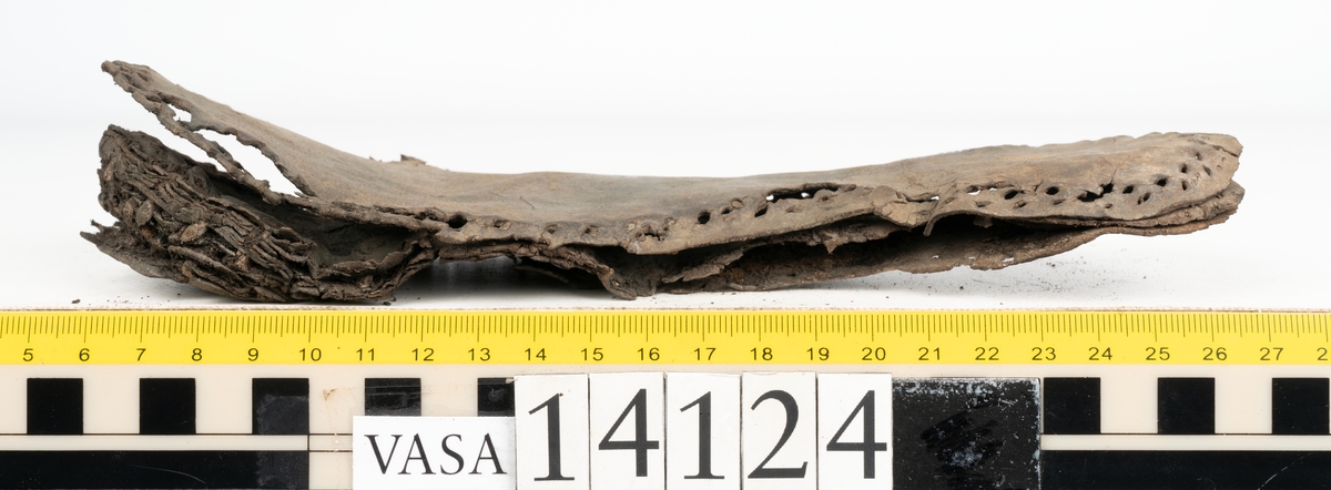 Sandalsydd högersko, troligtvis toffel, i delar.

Skobottnen består av två sulor med kvarsittanda skopligg och tråd. Vid tåpartiet sitter laglappar. På undersidan av yttersulan syns rostfärgade utfällningar.

Elva fragment från bottnen: sulor m m.

Ett fragmentariskt ovanläder. Ovanlädret har vita och rostfärgade utfällningar samt ligger hopvikt. Lädret är mycket sprött.
Totalt 15 fragment.