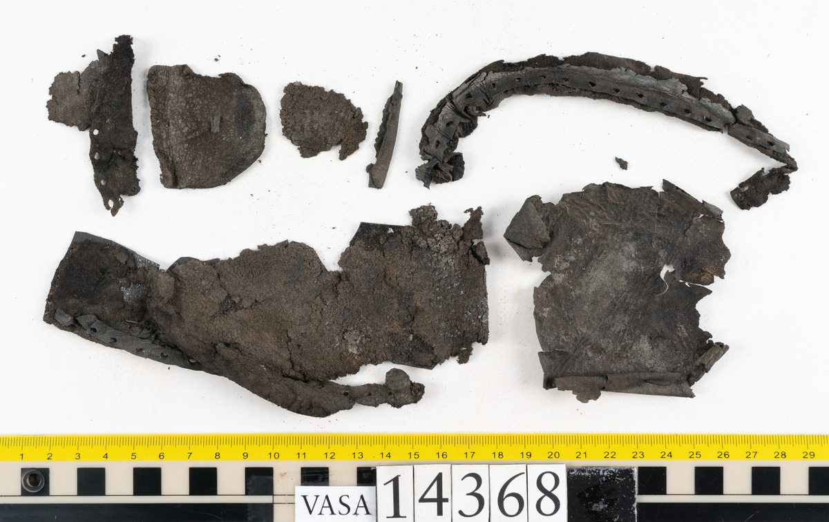 Dokumentation 1996:
Delar av sko: skobotten samt ett trettiotal fragment av ovanläder, holtrand m m.
Skobottnen består av tre sulor, holtrand och sex klacklappar. Mellan två av sulorna sitter klacklapparna fästade. En del av bakkappan sitter fästad vid bottnen.  Bottnen har kvarsittande tråd och vid hälpartiet finns kvarsittande skopligg.

Dokumentation 2022:
Skobotten till en randsko. Tillverkad i läder, med en läderklack. Skapades på en rak läst och bars på vänster fot. Inga dekorationer. Mittensulorna är delaminerade och är skurna längst med deras mittenpunkt. Randen är intakt och tå-delen är unik. 
För mer information, se Uppritning under Länkade filer.

Text in english:
This is the bottom unit of a shoe, made of leather, randed construction with a spring heel, made on a straight last and worn on the left foot, with no decorative features. The two midsoles are heavily delaminated and there is a slice along the centre of the sole. The rand is intact, and the toe wear is unique.
For more information, go to Länkade filer: Uppritning