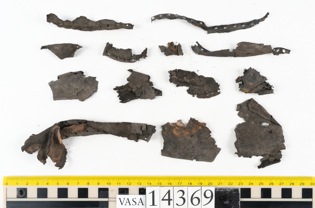 Delar och fragment från holtrandsydd sko: del av skobotten, två sulor samt ett 20-tal fragment från bottnen.

Skobottnen bestående av två sulor, rand och tre klacklappar. Bottnen har kvarsittande tråd och skopligg. Lädret är kraftigt.

En sula tillhörande skobottnen. Runt ytterkanten finns kvarsittande, grov, tråd. Lädret är kraftigt.  Det är något osäkert om den andra sulan hör till ovan skobotten.

Flertalet fragment har rostfärgade utfällningar.
