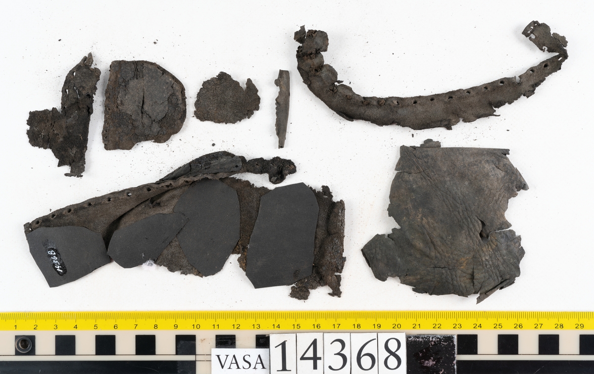 Dokumentation 1996:
Delar av sko: skobotten samt ett trettiotal fragment av ovanläder, holtrand m m.
Skobottnen består av tre sulor, holtrand och sex klacklappar. Mellan två av sulorna sitter klacklapparna fästade. En del av bakkappan sitter fästad vid bottnen.  Bottnen har kvarsittande tråd och vid hälpartiet finns kvarsittande skopligg.

Dokumentation 2022:
Skobotten till en randsko. Tillverkad i läder, med en läderklack. Skapades på en rak läst och bars på vänster fot. Inga dekorationer. Mittensulorna är delaminerade och är skurna längst med deras mittenpunkt. Randen är intakt och tå-delen är unik. 
För mer information, se Uppritning under Länkade filer.

Text in english:
This is the bottom unit of a shoe, made of leather, randed construction with a spring heel, made on a straight last and worn on the left foot, with no decorative features. The two midsoles are heavily delaminated and there is a slice along the centre of the sole. The rand is intact, and the toe wear is unique.
For more information, go to Länkade filer: Uppritning