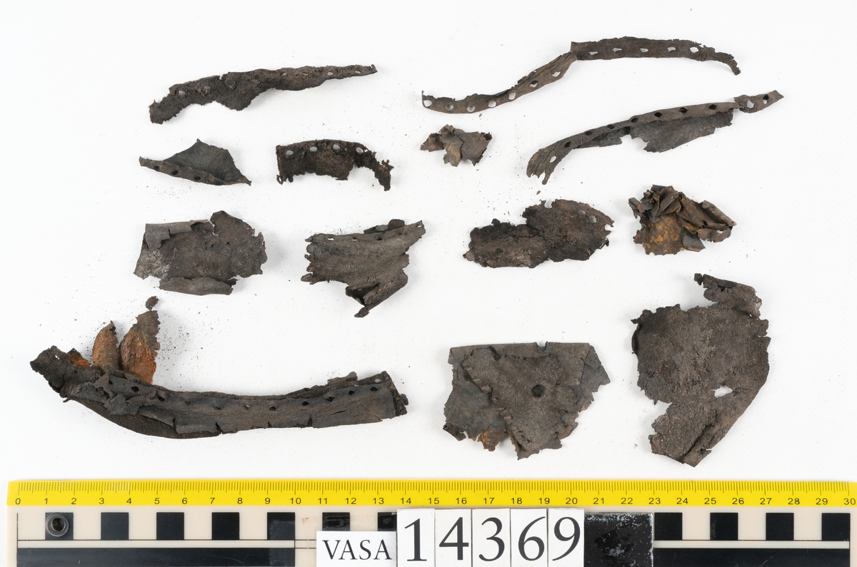 Delar och fragment från holtrandsydd sko: del av skobotten, två sulor samt ett 20-tal fragment från bottnen.

Skobottnen bestående av två sulor, rand och tre klacklappar. Bottnen har kvarsittande tråd och skopligg. Lädret är kraftigt.

En sula tillhörande skobottnen. Runt ytterkanten finns kvarsittande, grov, tråd. Lädret är kraftigt.  Det är något osäkert om den andra sulan hör till ovan skobotten.

Flertalet fragment har rostfärgade utfällningar.