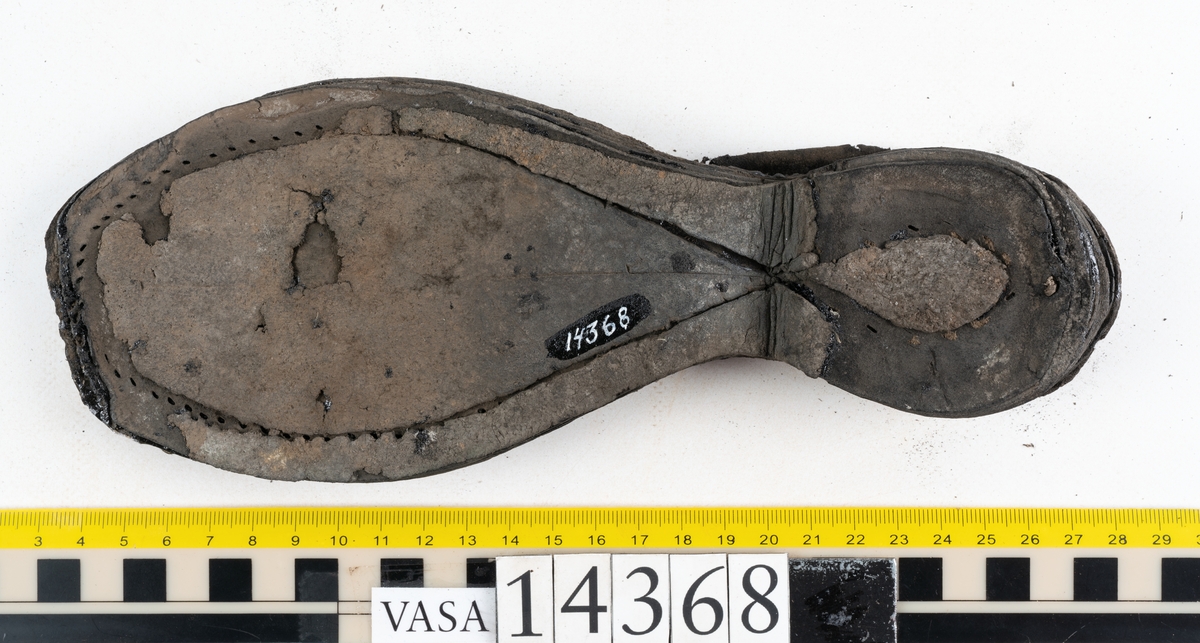 Dokumentation 1996:
Delar av sko: skobotten samt ett trettiotal fragment av ovanläder, holtrand m m.
Skobottnen består av tre sulor, holtrand och sex klacklappar. Mellan två av sulorna sitter klacklapparna fästade. En del av bakkappan sitter fästad vid bottnen.  Bottnen har kvarsittande tråd och vid hälpartiet finns kvarsittande skopligg.

Dokumentation 2022:
Skobotten till en randsko. Tillverkad i läder, med en läderklack. Skapades på en rak läst och bars på vänster fot. Inga dekorationer. Mittensulorna är delaminerade och är skurna längst med deras mittenpunkt. Randen är intakt och tå-delen är unik. 
För mer information, se Uppritning under Länkade filer.

Text in english:
This is the bottom unit of a shoe, made of leather, randed construction with a spring heel, made on a straight last and worn on the left foot, with no decorative features. The two midsoles are heavily delaminated and there is a slice along the centre of the sole. The rand is intact, and the toe wear is unique.
For more information, go to Länkade filer: Uppritning