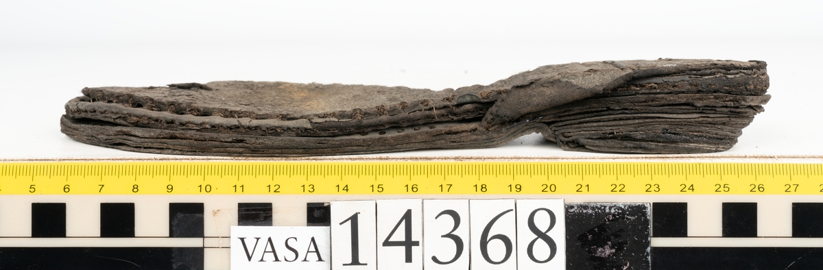 Dokumentation 1996:
Delar av sko: skobotten samt ett trettiotal fragment av ovanläder, holtrand m m.
Skobottnen består av tre sulor, holtrand och sex klacklappar. Mellan två av sulorna sitter klacklapparna fästade. En del av bakkappan sitter fästad vid bottnen.  Bottnen har kvarsittande tråd och vid hälpartiet finns kvarsittande skopligg.

Dokumentation 2022:
Skobotten till en randsko. Tillverkad i läder, med en läderklack. Skapades på en rak läst och bars på vänster fot. Inga dekorationer. Mittensulorna är delaminerade och är skurna längst med deras mittenpunkt. Randen är intakt och tå-delen är unik. 
För mer information, se Uppritning under Länkade filer.

Text in english:
This is the bottom unit of a shoe, made of leather, randed construction with a spring heel, made on a straight last and worn on the left foot, with no decorative features. The two midsoles are heavily delaminated and there is a slice along the centre of the sole. The rand is intact, and the toe wear is unique.
For more information, go to Länkade filer: Uppritning