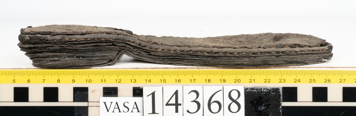 Dokumentation 1996:
Delar av sko: skobotten samt ett trettiotal fragment av ovanläder, holtrand m m.
Skobottnen består av tre sulor, holtrand och sex klacklappar. Mellan två av sulorna sitter klacklapparna fästade. En del av bakkappan sitter fästad vid bottnen.  Bottnen har kvarsittande tråd och vid hälpartiet finns kvarsittande skopligg.

Dokumentation 2022:
Skobotten till en randsko. Tillverkad i läder, med en läderklack. Skapades på en rak läst och bars på vänster fot. Inga dekorationer. Mittensulorna är delaminerade och är skurna längst med deras mittenpunkt. Randen är intakt och tå-delen är unik. 
För mer information, se Uppritning under Länkade filer.

Text in english:
This is the bottom unit of a shoe, made of leather, randed construction with a spring heel, made on a straight last and worn on the left foot, with no decorative features. The two midsoles are heavily delaminated and there is a slice along the centre of the sole. The rand is intact, and the toe wear is unique.
For more information, go to Länkade filer: Uppritning