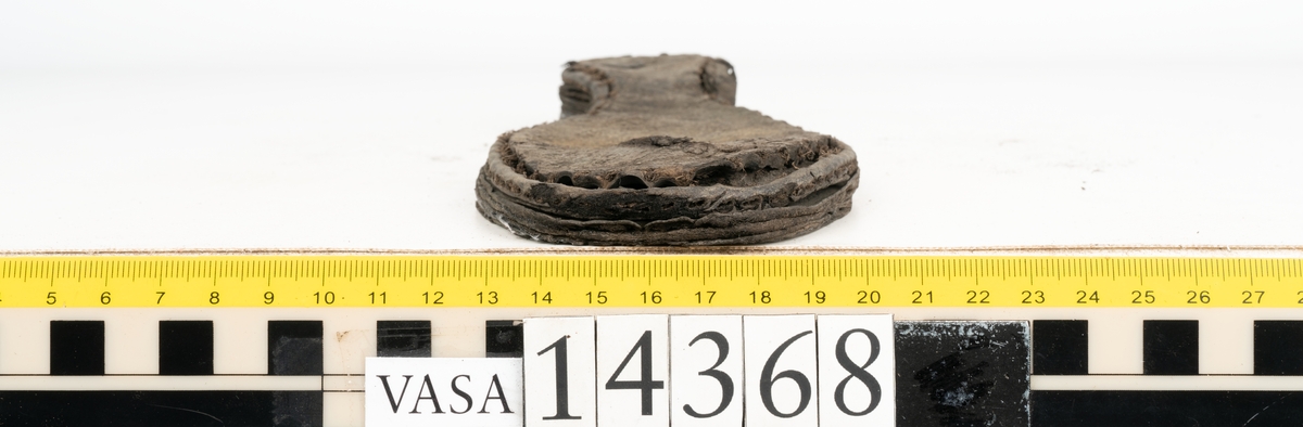 Dokumentation 1996:
Delar av sko: skobotten samt ett trettiotal fragment av ovanläder, holtrand m m.
Skobottnen består av tre sulor, holtrand och sex klacklappar. Mellan två av sulorna sitter klacklapparna fästade. En del av bakkappan sitter fästad vid bottnen.  Bottnen har kvarsittande tråd och vid hälpartiet finns kvarsittande skopligg.

Dokumentation 2022:
Skobotten till en randsko. Tillverkad i läder, med en läderklack. Skapades på en rak läst och bars på vänster fot. Inga dekorationer. Mittensulorna är delaminerade och är skurna längst med deras mittenpunkt. Randen är intakt och tå-delen är unik. 
För mer information, se Uppritning under Länkade filer.

Text in english:
This is the bottom unit of a shoe, made of leather, randed construction with a spring heel, made on a straight last and worn on the left foot, with no decorative features. The two midsoles are heavily delaminated and there is a slice along the centre of the sole. The rand is intact, and the toe wear is unique.
For more information, go to Länkade filer: Uppritning