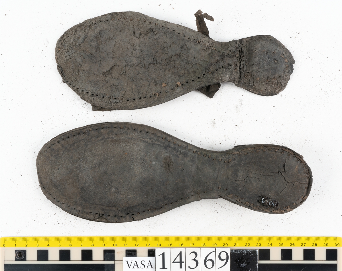 Delar och fragment från holtrandsydd sko: del av skobotten, två sulor samt ett 20-tal fragment från bottnen.

Skobottnen bestående av två sulor, rand och tre klacklappar. Bottnen har kvarsittande tråd och skopligg. Lädret är kraftigt.

En sula tillhörande skobottnen. Runt ytterkanten finns kvarsittande, grov, tråd. Lädret är kraftigt.  Det är något osäkert om den andra sulan hör till ovan skobotten.

Flertalet fragment har rostfärgade utfällningar.