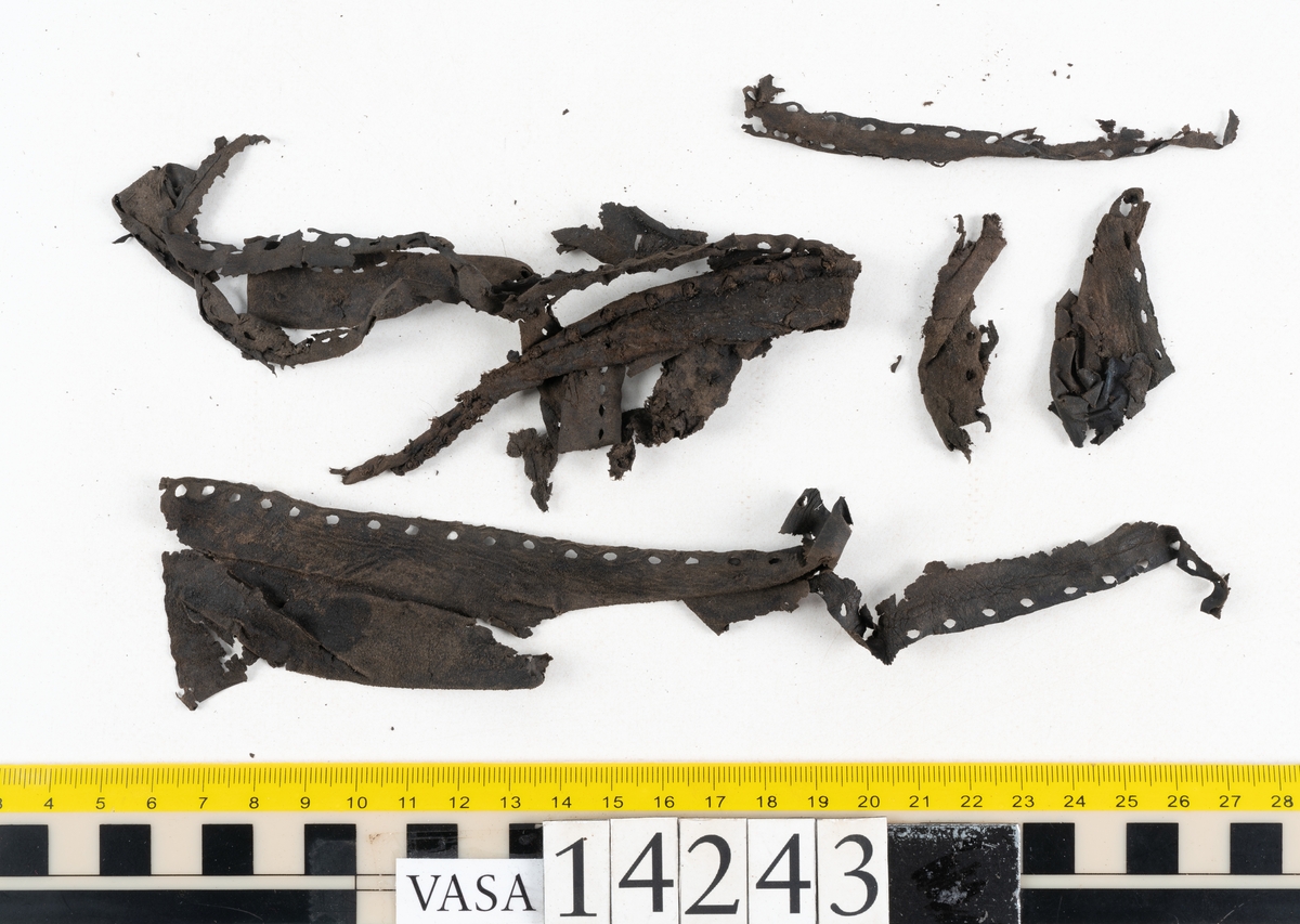 Två bottnar samt ovanläder till ett par skor. Troligtvis är skorna sandalsydda.
Botten till högersko, fyndnummer 14243. I stygnshålen finns kvarsittande tråd och på undersidan av hälpartiet finns kvarsittande skopligg.
Botten till vänstersko, fyndnummer 14243:1. I stygnshålen finns kvarsittande tråd. På klackens undersida finns en laglapp med kvarsittande träpligg.
Ovanlädret består av större och mindre bitar. Lädret är mycket sprött.
Totalt omfattar fynder ett 60-tal fragment.