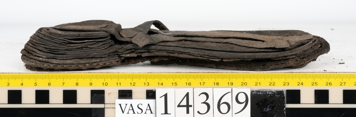 Delar och fragment från holtrandsydd sko: del av skobotten, två sulor samt ett 20-tal fragment från bottnen.

Skobottnen bestående av två sulor, rand och tre klacklappar. Bottnen har kvarsittande tråd och skopligg. Lädret är kraftigt.

En sula tillhörande skobottnen. Runt ytterkanten finns kvarsittande, grov, tråd. Lädret är kraftigt.  Det är något osäkert om den andra sulan hör till ovan skobotten.

Flertalet fragment har rostfärgade utfällningar.