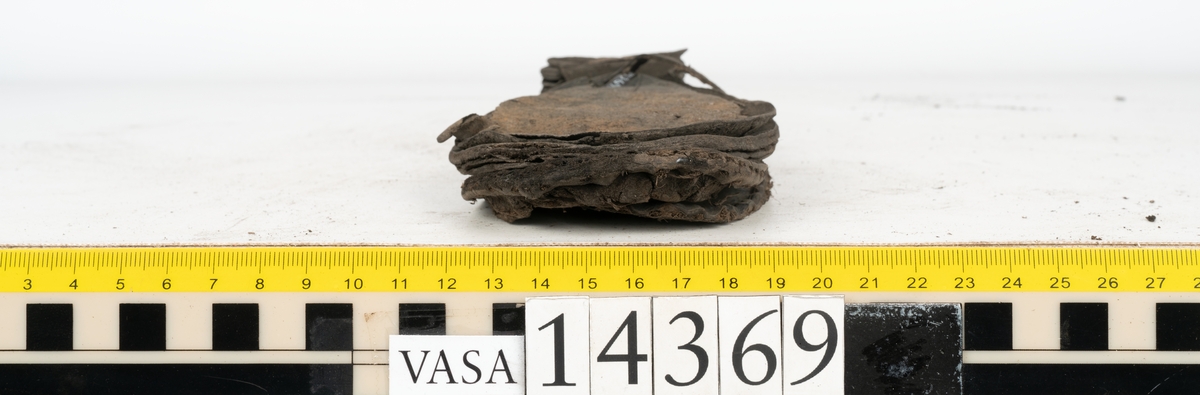 Delar och fragment från holtrandsydd sko: del av skobotten, två sulor samt ett 20-tal fragment från bottnen.

Skobottnen bestående av två sulor, rand och tre klacklappar. Bottnen har kvarsittande tråd och skopligg. Lädret är kraftigt.

En sula tillhörande skobottnen. Runt ytterkanten finns kvarsittande, grov, tråd. Lädret är kraftigt.  Det är något osäkert om den andra sulan hör till ovan skobotten.

Flertalet fragment har rostfärgade utfällningar.