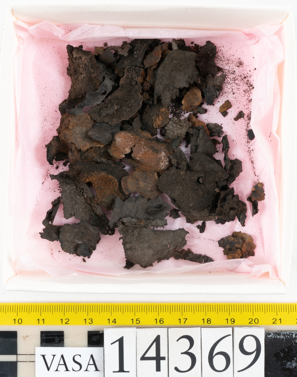 Delar och fragment från holtrandsydd sko: del av skobotten, två sulor samt ett 20-tal fragment från bottnen.

Skobottnen bestående av två sulor, rand och tre klacklappar. Bottnen har kvarsittande tråd och skopligg. Lädret är kraftigt.

En sula tillhörande skobottnen. Runt ytterkanten finns kvarsittande, grov, tråd. Lädret är kraftigt.  Det är något osäkert om den andra sulan hör till ovan skobotten.

Flertalet fragment har rostfärgade utfällningar.