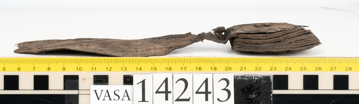 Två bottnar samt ovanläder till ett par skor. Troligtvis är skorna sandalsydda.
Botten till högersko, fyndnummer 14243. I stygnshålen finns kvarsittande tråd och på undersidan av hälpartiet finns kvarsittande skopligg.
Botten till vänstersko, fyndnummer 14243:1. I stygnshålen finns kvarsittande tråd. På klackens undersida finns en laglapp med kvarsittande träpligg.
Ovanlädret består av större och mindre bitar. Lädret är mycket sprött.
Totalt omfattar fynder ett 60-tal fragment.