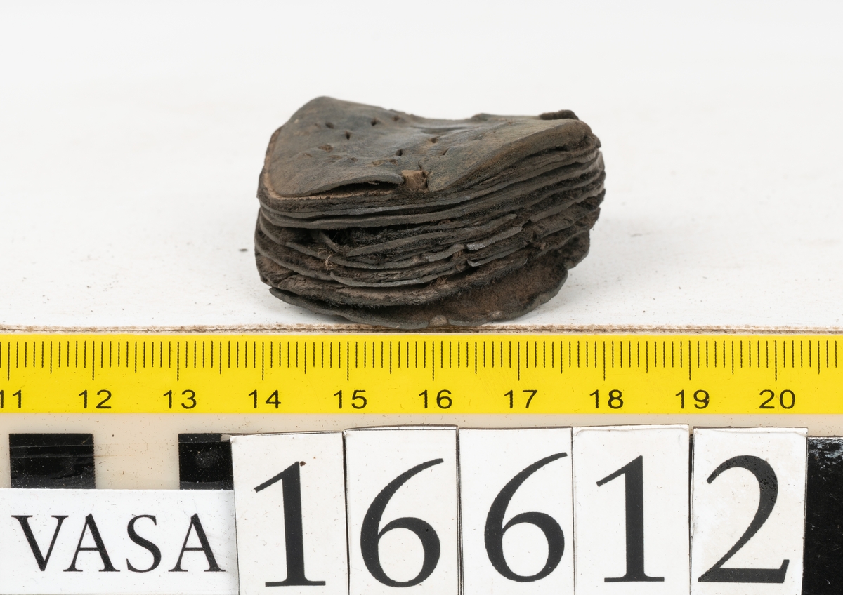 Delar och fragment av två skobottnar till höger- och vänstersko. Totalt 18 delar och fragment.
Sju sulor med kvarsittande tråd. Sulornas längd varierar mellan 220-230 mm, största bredden varierar mellan 65-75 mm, minsta bredden mellan 25-35 mm och hälbredden mellan 45-50 mm. Lädret till sulorna är kraftigt.
Klackar 16612 samt 16612:1 består av vardera fem klacklappar med kvarsittandskopligg. Klacklapparna är spaltade. I materialet finns en löst liggande klacklapp som tillhör klack 16621:1.
Tre delar holtrand med kvarsittande tråd.
Tre fragment från skobotten.