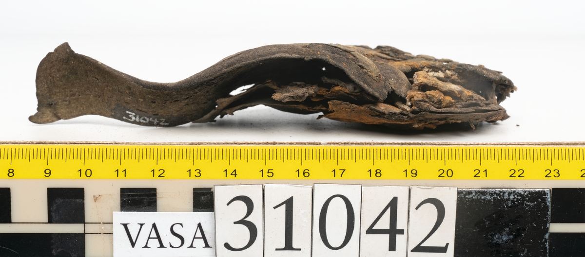 Del av en skobotten samt två fragmentariska sulor. Totalt ett tiotal fragment. Bottnens klackparti är fragmentariskt. På undersidan sitter halvmånformade laglappar. Kvarsittande skopligg. Lädret har rostfärgade utfällningar.