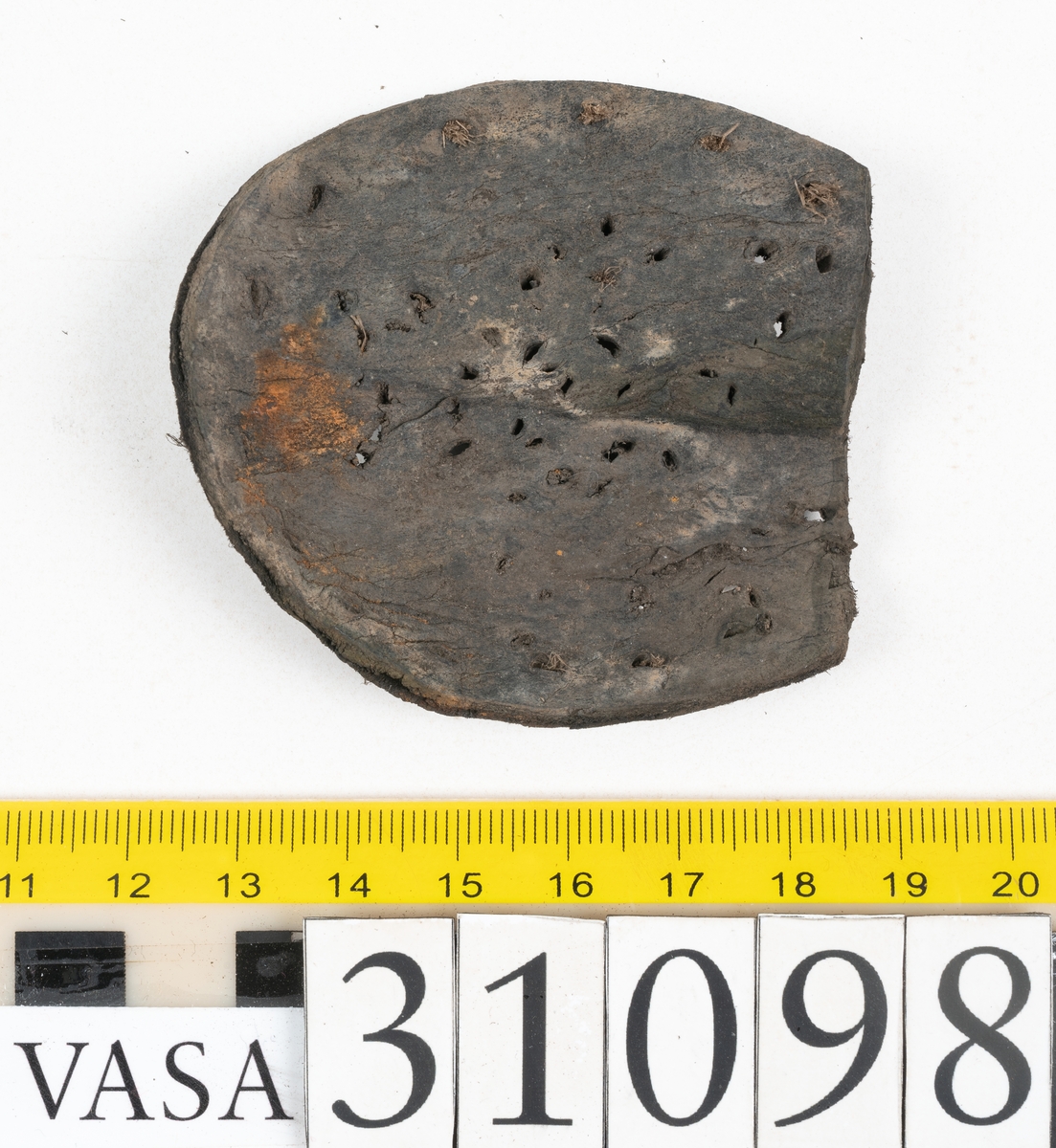 Dokumentation 1997:
Tre delar av sko: en del av en skobotten, en klacklapp och ett ovanläder samt två fragment som lossnat från dessa.
Del av skobotten i form av en yttersula med kvarsittande klack. Klacken är uppbyggd av 5-6 klacklappar. Sulans undersida är ritsad. Sulan är spaltad och tåpartiet är fragmentarisk. Sulan och klacken har kvarsittande träpligg.
En klacklapp med kvarsittande träpligg. Runt ytterkanterna och i klacklappens mitt finns hål efter träpligg.
Ett ovanläder samt en lös bit av plösen. På den lösa biten finns två snörhål. Längs med ovanlädrets ytterkanter löper stygnshål. Köttsidan har börjat att släppa från narvsidan.

Dokumentation 2022:
Del av ovanläder. Framstycke till en öppen svensksko som består av fragment. Tillverkad i läder. Inga dekorationer. Tillhörde en sko som bars på vänster fot. Ovanligt spetsig tå-del. Plösen är skadad och saknas. Det finns delaminering och veckning och inga tecken på lagningar. Det finns en tillhörande klack.
För mer information, se Länkade filer: Uppritning

Text in english:
This is the vamp of an open latchet shoe, made of leather, of stitch-down construction, worn on the left foot, with no decorative features, and an unusually pointed toe. The vamp consists of fragments, with the tongue broken off, and has suffered delamination and creasing. There are no signs of repairs. There is a heel associated with the vamp.
For more information, go to Länkade filer: Uppritning
