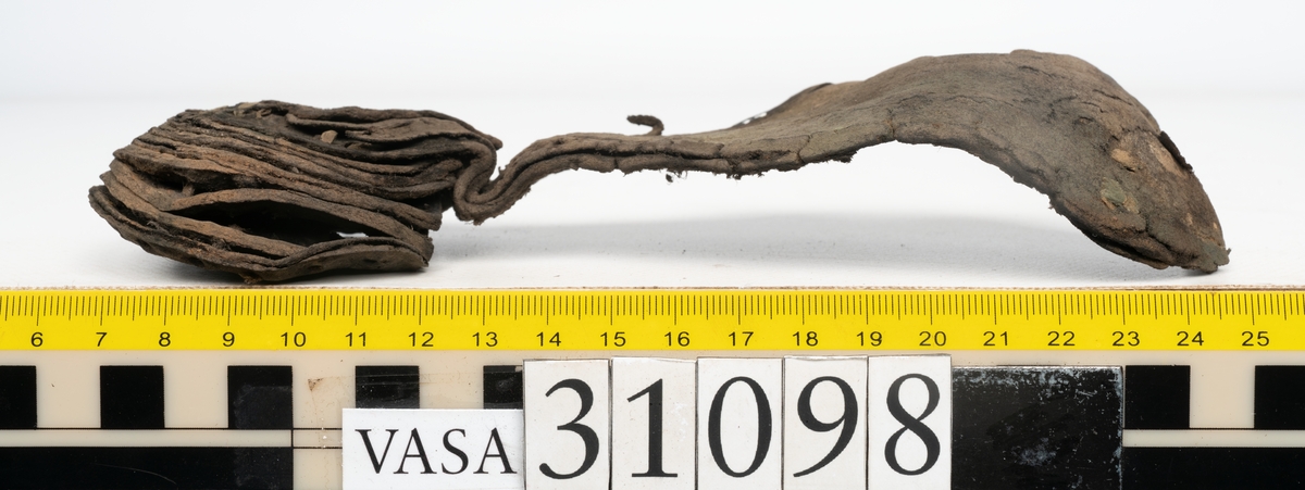 Dokumentation 1997:
Tre delar av sko: en del av en skobotten, en klacklapp och ett ovanläder samt två fragment som lossnat från dessa.
Del av skobotten i form av en yttersula med kvarsittande klack. Klacken är uppbyggd av 5-6 klacklappar. Sulans undersida är ritsad. Sulan är spaltad och tåpartiet är fragmentarisk. Sulan och klacken har kvarsittande träpligg.
En klacklapp med kvarsittande träpligg. Runt ytterkanterna och i klacklappens mitt finns hål efter träpligg.
Ett ovanläder samt en lös bit av plösen. På den lösa biten finns två snörhål. Längs med ovanlädrets ytterkanter löper stygnshål. Köttsidan har börjat att släppa från narvsidan.

Dokumentation 2022:
Del av ovanläder. Framstycke till en öppen svensksko som består av fragment. Tillverkad i läder. Inga dekorationer. Tillhörde en sko som bars på vänster fot. Ovanligt spetsig tå-del. Plösen är skadad och saknas. Det finns delaminering och veckning och inga tecken på lagningar. Det finns en tillhörande klack.
För mer information, se Länkade filer: Uppritning

Text in english:
This is the vamp of an open latchet shoe, made of leather, of stitch-down construction, worn on the left foot, with no decorative features, and an unusually pointed toe. The vamp consists of fragments, with the tongue broken off, and has suffered delamination and creasing. There are no signs of repairs. There is a heel associated with the vamp.
For more information, go to Länkade filer: Uppritning