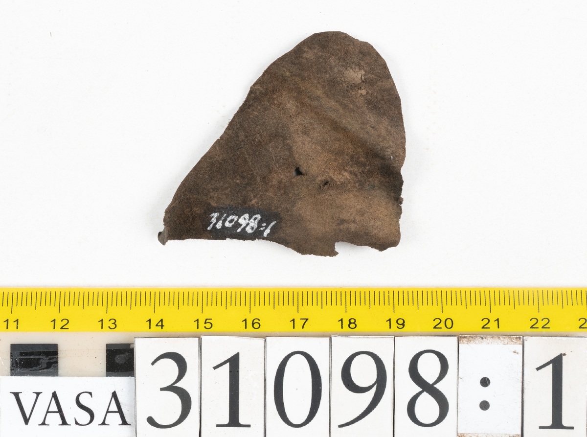 Dokumentation 1997:
Tre delar av sko: en del av en skobotten, en klacklapp och ett ovanläder samt två fragment som lossnat från dessa.
Del av skobotten i form av en yttersula med kvarsittande klack. Klacken är uppbyggd av 5-6 klacklappar. Sulans undersida är ritsad. Sulan är spaltad och tåpartiet är fragmentarisk. Sulan och klacken har kvarsittande träpligg.
En klacklapp med kvarsittande träpligg. Runt ytterkanterna och i klacklappens mitt finns hål efter träpligg.
Ett ovanläder samt en lös bit av plösen. På den lösa biten finns två snörhål. Längs med ovanlädrets ytterkanter löper stygnshål. Köttsidan har börjat att släppa från narvsidan.

Dokumentation 2022:
Del av ovanläder. Framstycke till en öppen svensksko som består av fragment. Tillverkad i läder. Inga dekorationer. Tillhörde en sko som bars på vänster fot. Ovanligt spetsig tå-del. Plösen är skadad och saknas. Det finns delaminering och veckning och inga tecken på lagningar. Det finns en tillhörande klack.
För mer information, se Länkade filer: Uppritning

Text in english:
This is the vamp of an open latchet shoe, made of leather, of stitch-down construction, worn on the left foot, with no decorative features, and an unusually pointed toe. The vamp consists of fragments, with the tongue broken off, and has suffered delamination and creasing. There are no signs of repairs. There is a heel associated with the vamp.
For more information, go to Länkade filer: Uppritning